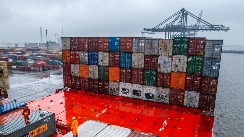 A busy container terminal with dock workers and shipping containers during rainy weather., tags: de en - pexel